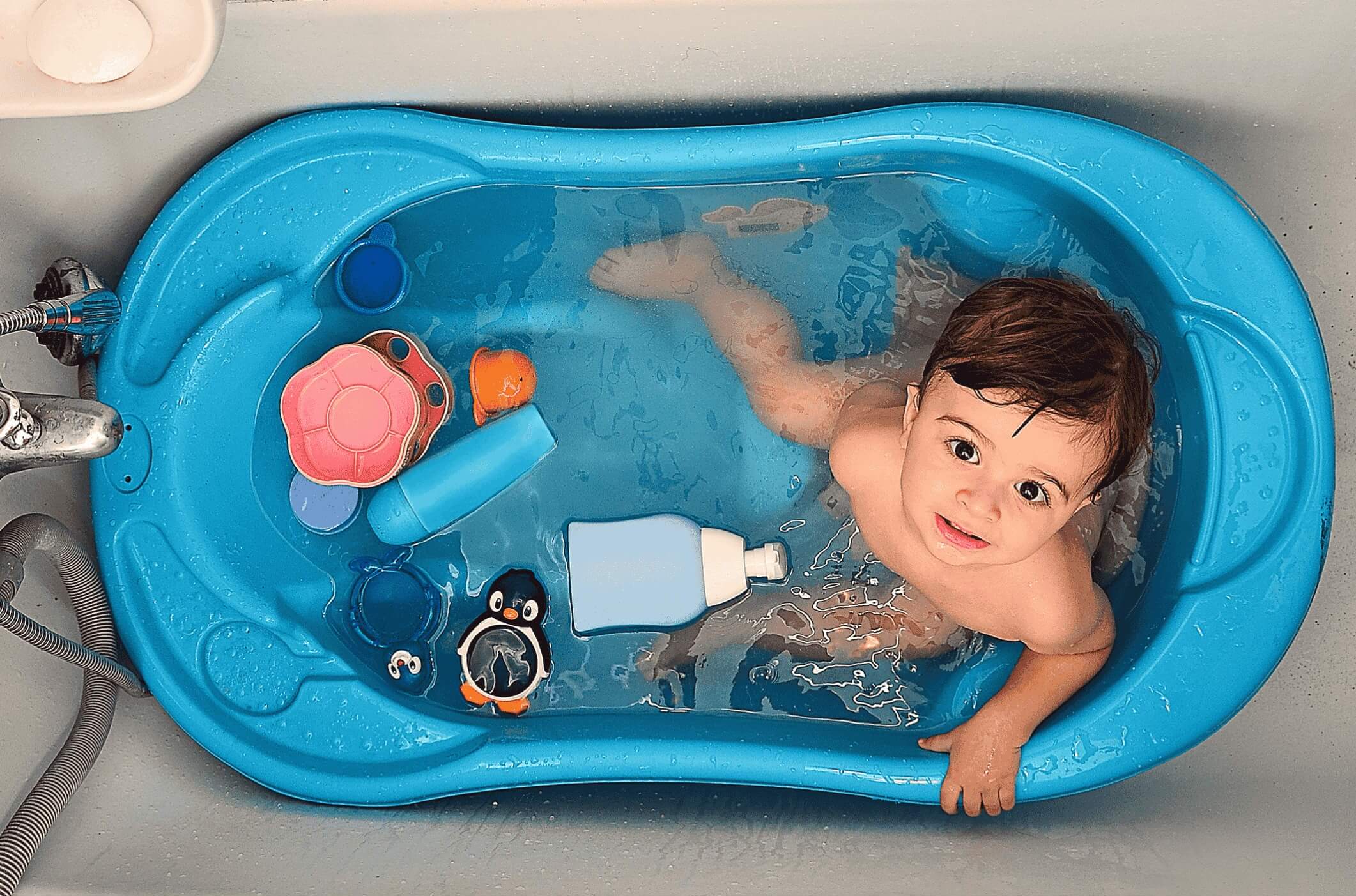 Happy baby getting a gentle hair rinse with bottled water—made easier with The Gulf Shower for bath time comfort.